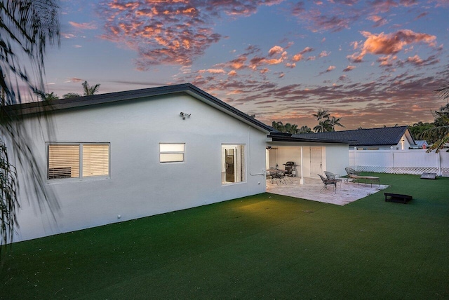 back house at dusk featuring a patio and a lawn