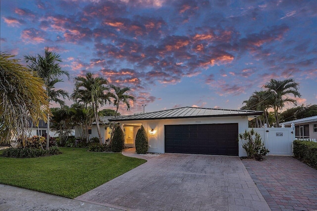 view of front of property featuring stucco siding, a standing seam roof, a garage, decorative driveway, and a front yard