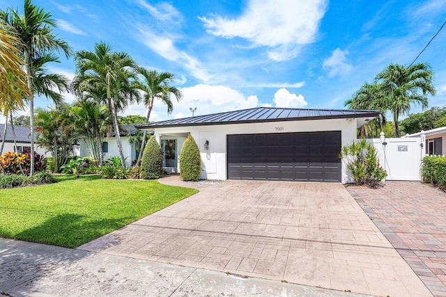 ranch-style home with metal roof, a front lawn, a standing seam roof, decorative driveway, and a garage