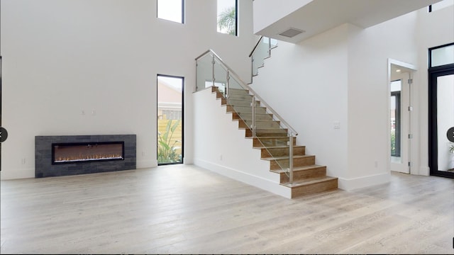 entryway featuring a high ceiling, a tiled fireplace, light wood-type flooring, and plenty of natural light