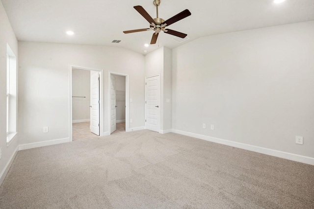 unfurnished bedroom with lofted ceiling, ensuite bathroom, a walk in closet, ceiling fan, and light colored carpet