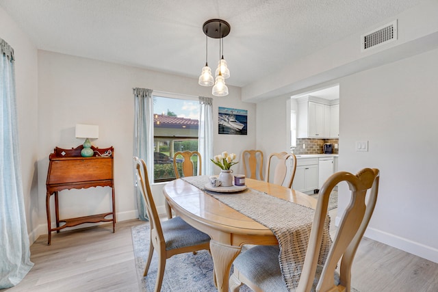 dining area with light hardwood / wood-style floors, a textured ceiling, and a chandelier