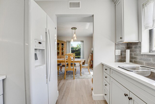 kitchen featuring white cabinetry, light hardwood / wood-style flooring, hanging light fixtures, white refrigerator with ice dispenser, and decorative backsplash