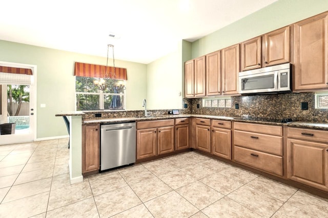 kitchen with stainless steel appliances, hanging light fixtures, sink, dark stone countertops, and kitchen peninsula