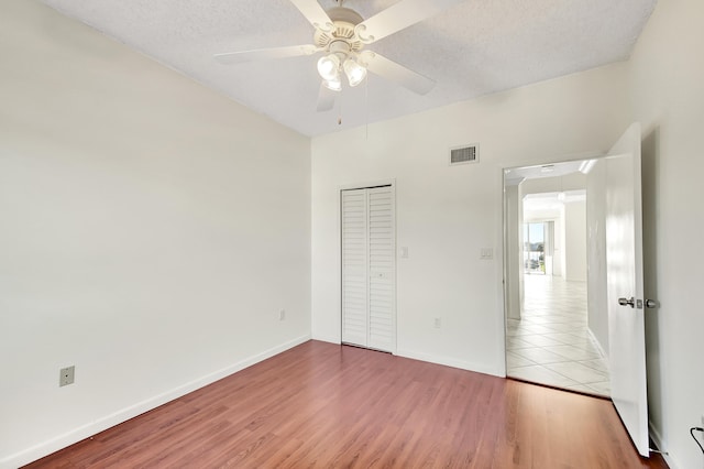 unfurnished bedroom featuring a textured ceiling, ceiling fan, a closet, and light wood-type flooring