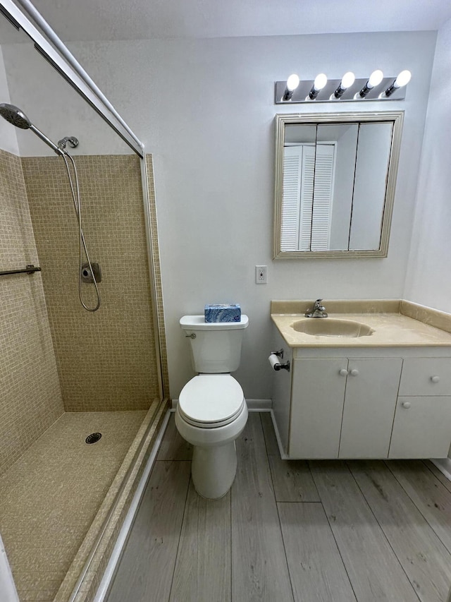 bathroom with a tile shower, vanity, wood-type flooring, and toilet