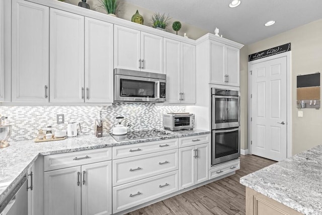 kitchen featuring white cabinets, light stone counters, light wood-type flooring, decorative backsplash, and appliances with stainless steel finishes