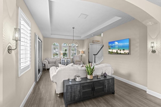 living room featuring a raised ceiling, an inviting chandelier, and dark wood-type flooring