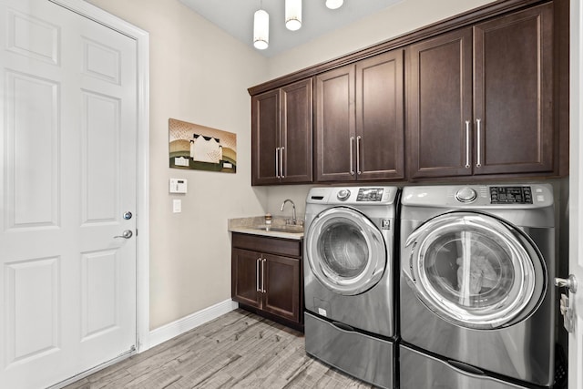 clothes washing area featuring light hardwood / wood-style floors, cabinets, washer and clothes dryer, and sink