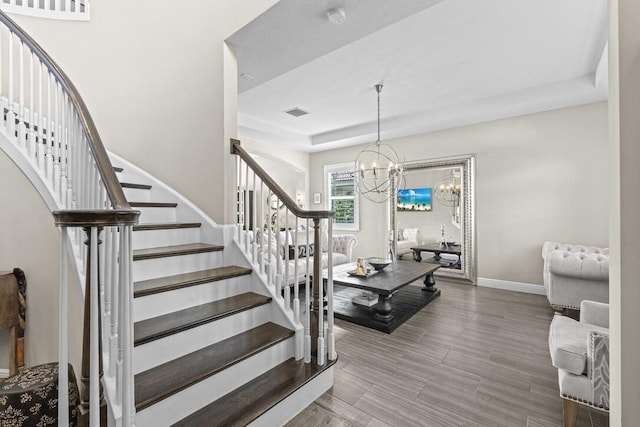 stairs featuring an inviting chandelier and a raised ceiling