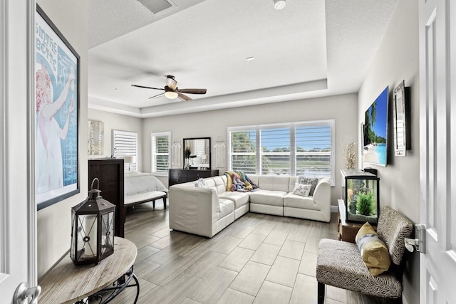 living room with a raised ceiling, a textured ceiling, and ceiling fan