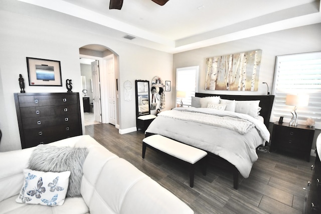 bedroom featuring dark wood-type flooring, a raised ceiling, ceiling fan, and multiple windows