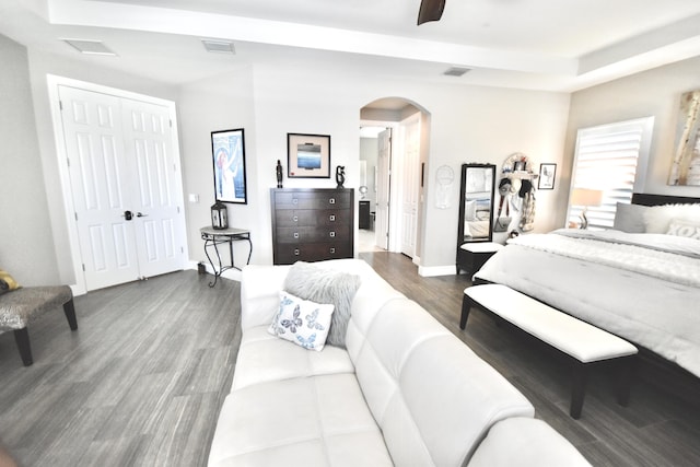 bedroom with a raised ceiling, ceiling fan, a closet, and dark hardwood / wood-style floors