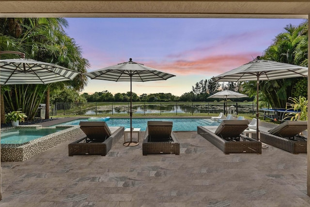 pool at dusk with a patio, pool water feature, an in ground hot tub, and a water view