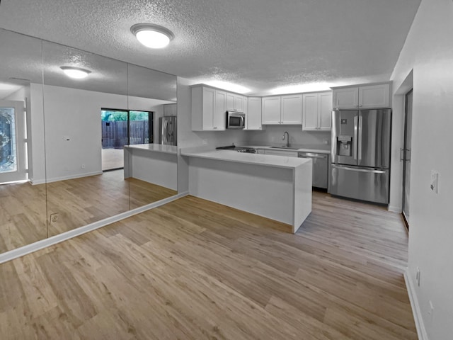 kitchen featuring sink, light hardwood / wood-style flooring, appliances with stainless steel finishes, white cabinetry, and kitchen peninsula