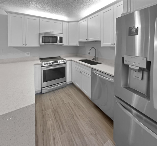 kitchen with sink, light wood-type flooring, white cabinets, and appliances with stainless steel finishes