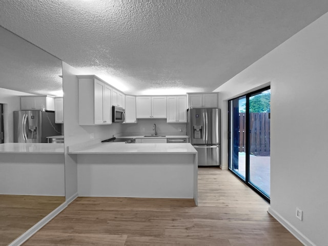 kitchen with light hardwood / wood-style flooring, stainless steel appliances, kitchen peninsula, and white cabinets