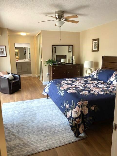 bedroom featuring ensuite bathroom, light wood-type flooring, ceiling fan, and a textured ceiling