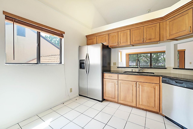 kitchen with lofted ceiling, sink, light tile patterned floors, dark stone countertops, and stainless steel appliances