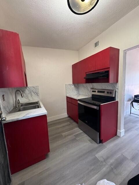 kitchen with extractor fan, stainless steel electric stove, light wood-type flooring, sink, and a textured ceiling