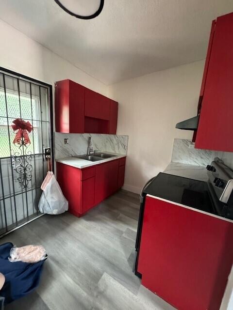 kitchen with stove, decorative backsplash, sink, and light wood-type flooring