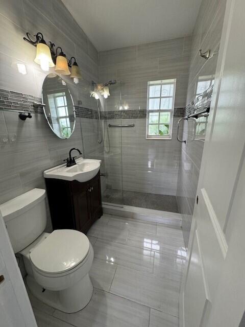 bathroom featuring vanity, tile patterned floors, tile walls, toilet, and a shower with door