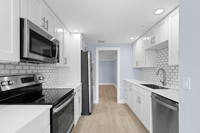 kitchen featuring stainless steel appliances, white cabinets, sink, backsplash, and light hardwood / wood-style flooring