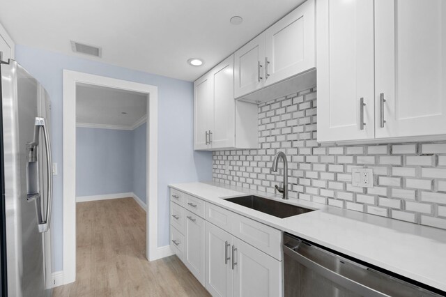 kitchen with stainless steel appliances, white cabinets, sink, backsplash, and light hardwood / wood-style floors