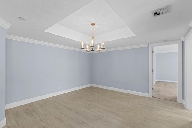 unfurnished room featuring baseboards, visible vents, an inviting chandelier, a tray ceiling, and light wood-style floors