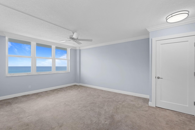 unfurnished room with light carpet, baseboards, a ceiling fan, ornamental molding, and a water view