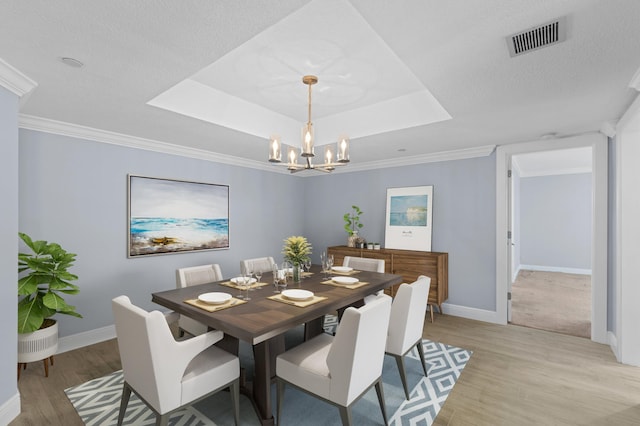 dining space featuring a tray ceiling, a chandelier, ornamental molding, and light hardwood / wood-style floors