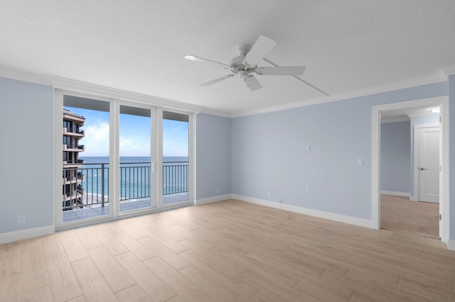 empty room with baseboards, light wood-style flooring, ceiling fan, a water view, and crown molding