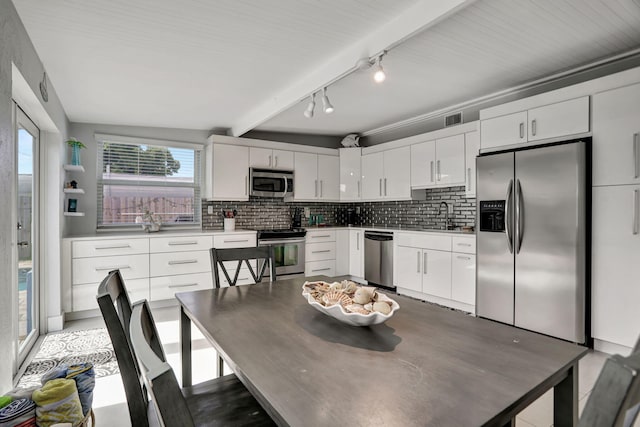 dining space featuring vaulted ceiling with beams, rail lighting, and sink