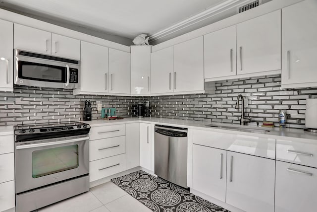 kitchen featuring light tile patterned floors, white cabinets, backsplash, stainless steel appliances, and sink