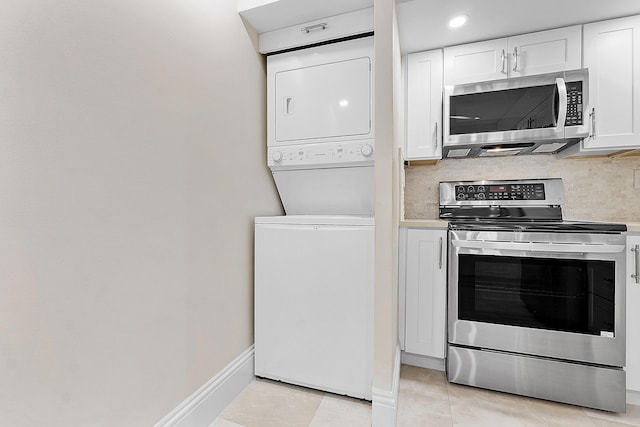 kitchen with stainless steel appliances, stacked washer / dryer, light countertops, and white cabinetry