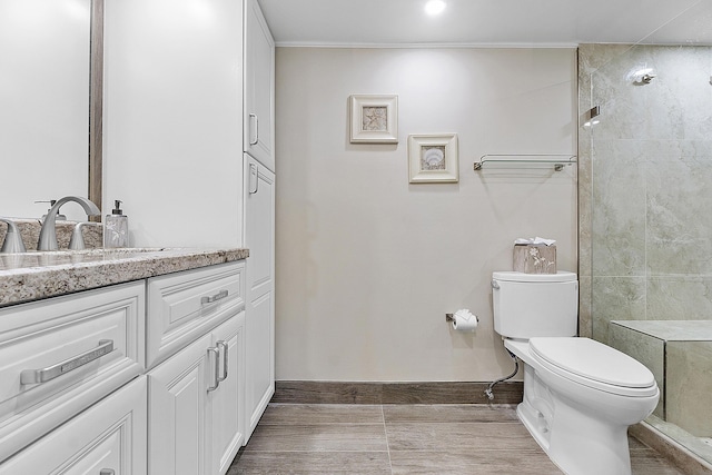 full bathroom featuring baseboards, a tile shower, vanity, and toilet