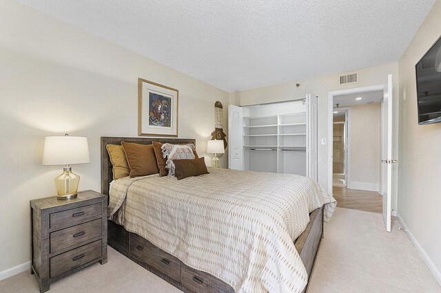 bedroom with a spacious closet, a textured ceiling, and light colored carpet