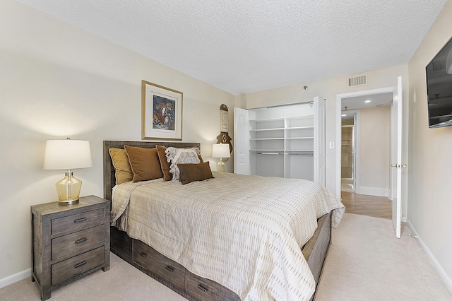 bedroom with visible vents, baseboards, a textured ceiling, and light colored carpet