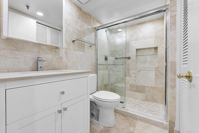 bathroom with tile walls, toilet, vanity, and a shower stall