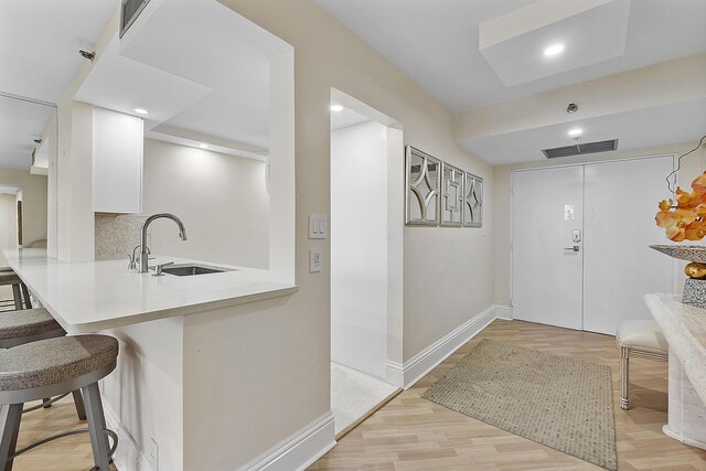 interior space with sink, a breakfast bar, light hardwood / wood-style floors, and white cabinetry