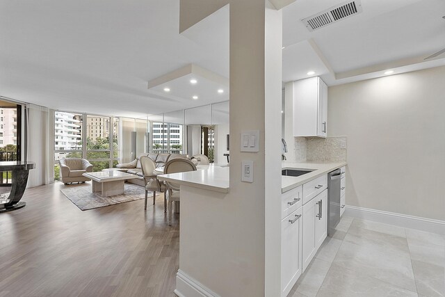 kitchen with white cabinetry, floor to ceiling windows, backsplash, dishwasher, and sink