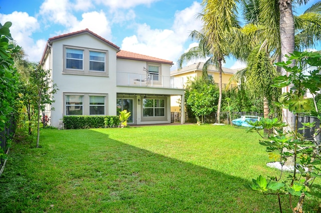 rear view of property with a yard, a swimming pool, and a balcony