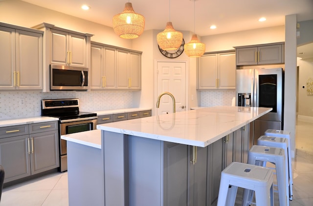 kitchen featuring a breakfast bar area, decorative light fixtures, appliances with stainless steel finishes, gray cabinets, and a kitchen island with sink