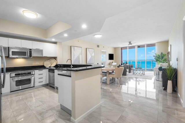 kitchen with appliances with stainless steel finishes, white cabinetry, a wall of windows, ceiling fan, and kitchen peninsula