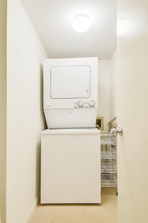 laundry area featuring light colored carpet and stacked washer / drying machine