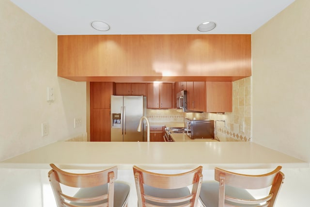 kitchen featuring appliances with stainless steel finishes, a breakfast bar, sink, kitchen peninsula, and decorative backsplash