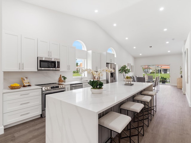 kitchen with appliances with stainless steel finishes, white cabinets, a kitchen island, decorative backsplash, and hardwood / wood-style flooring