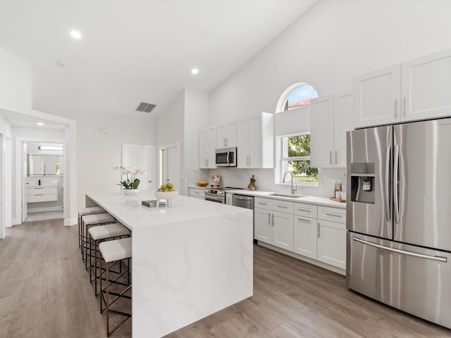 kitchen featuring light hardwood / wood-style flooring, stainless steel appliances, white cabinets, sink, and a center island