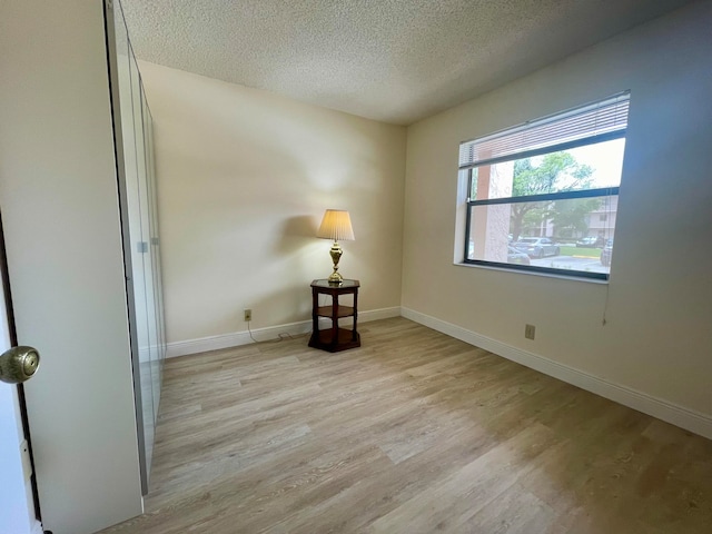 unfurnished room with light wood-type flooring and a textured ceiling