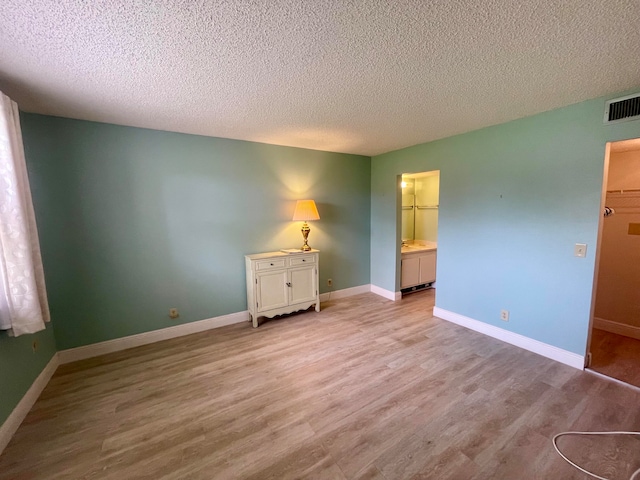 unfurnished bedroom with light hardwood / wood-style flooring, ensuite bath, and a textured ceiling